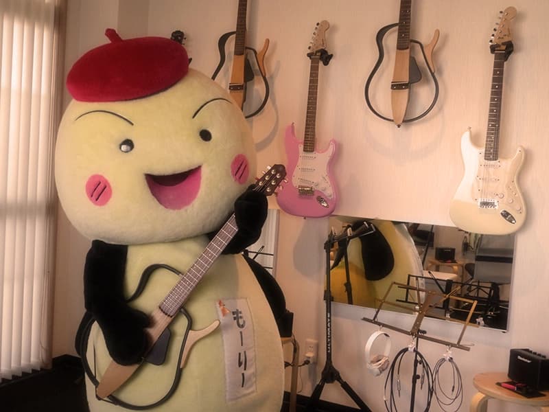 壁に並ぶギターと、教室に遊びに来たキャラクター「もーりー」